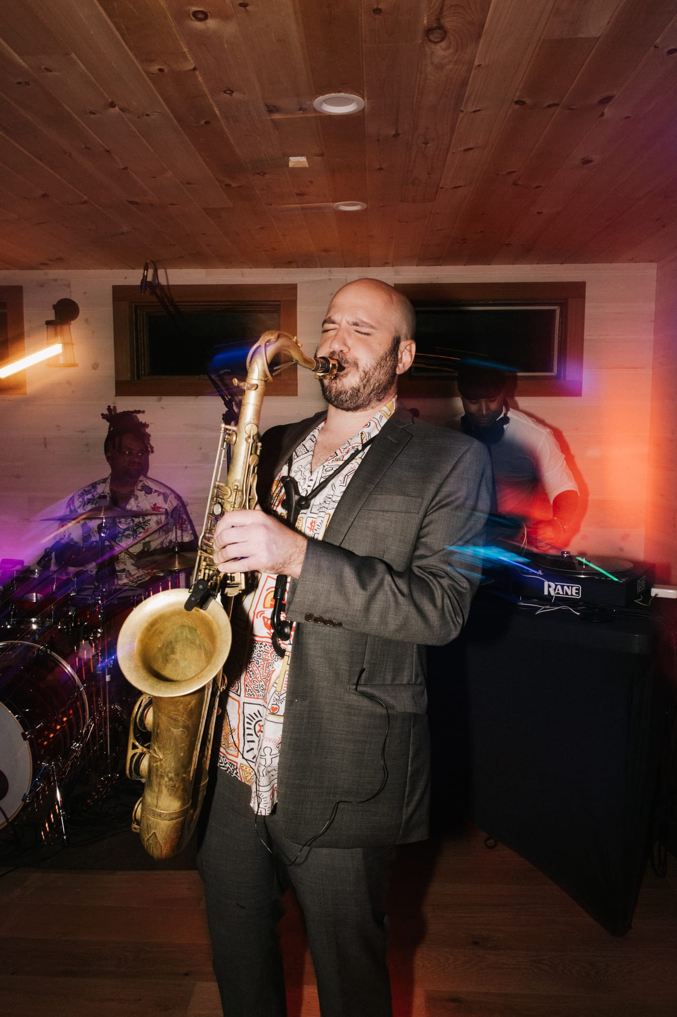 Saxophone player performing live with the DJ visible behind him
