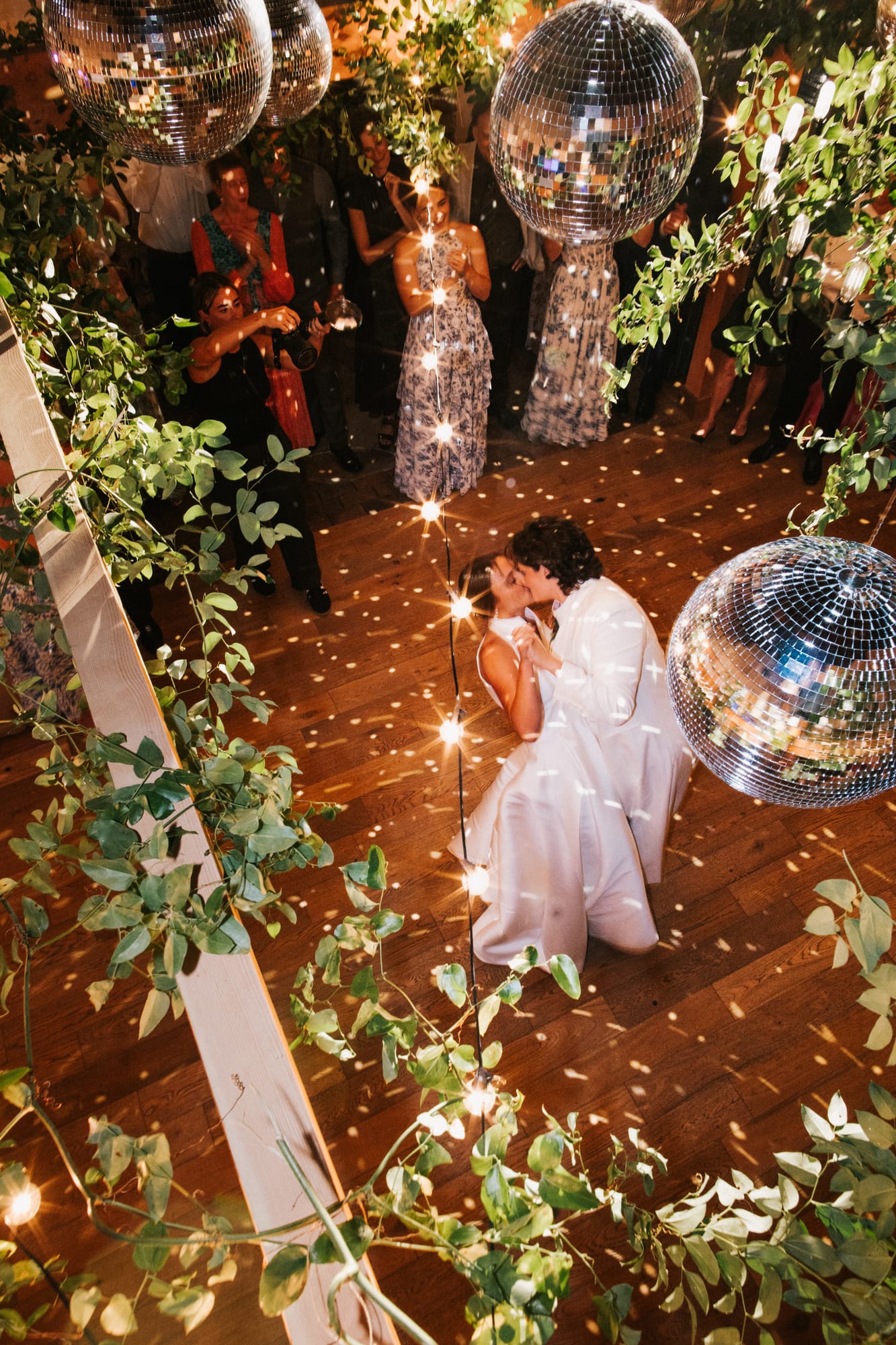 Two brides kissing on the dance floor under disco balls at their wedding